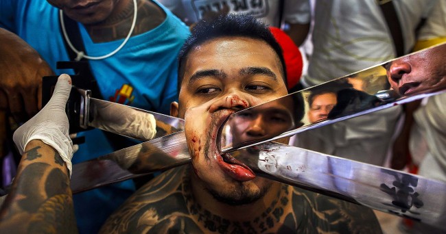 A devotee of the Chinese Bang Neow Shrine has another blade pierced through his cheek before a street procession during the annual vegetarian festival in Phuket