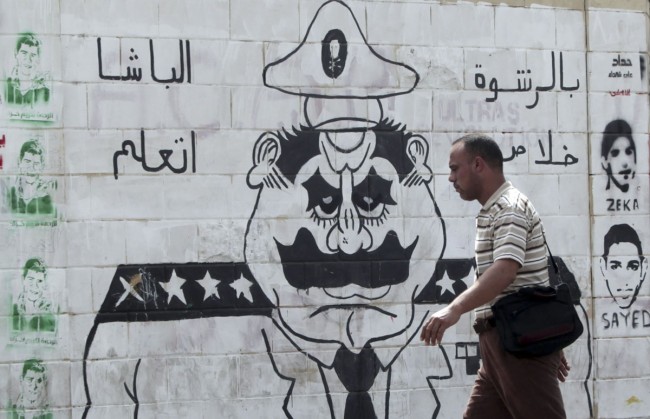 Egyptian man walks in front of a wall sprayed with anti-police graffiti in Cairo