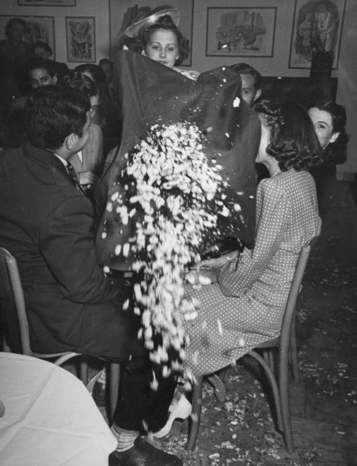 A woman throwing the crumbs from the tablecloth onto the floor.