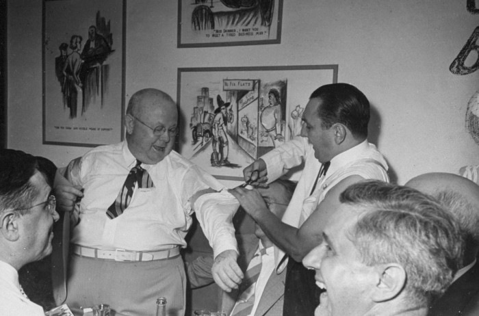 A gag waiter cutting the sleeve off a guest's shirt.