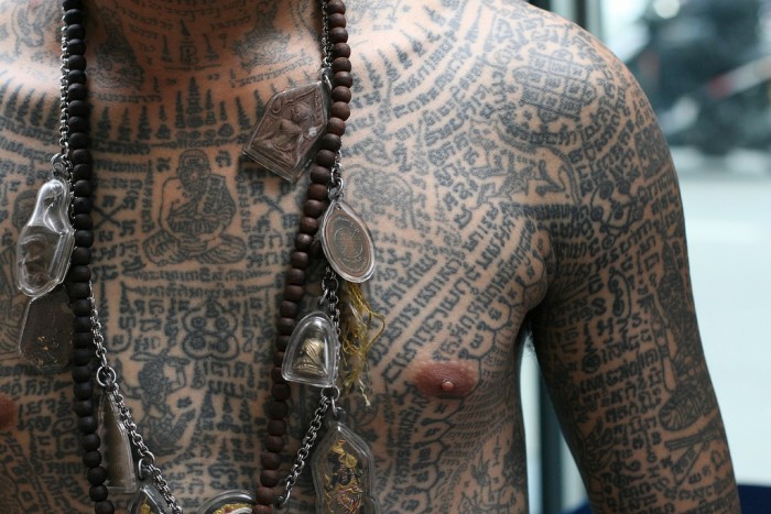A man covered in traditional Sak Yant tattoos and various magical amulets. 