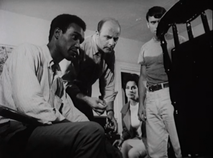 Survivors gather around a television screen, watching broadcast news media of the 1960s during the Night of the Living Dead, screenshot by the author.